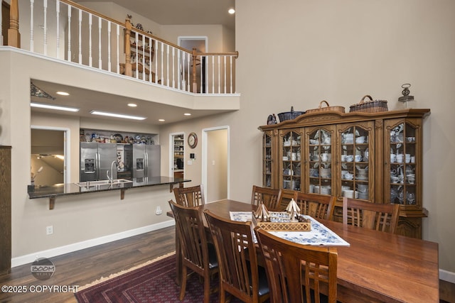 dining space featuring wood finished floors, baseboards, and a towering ceiling