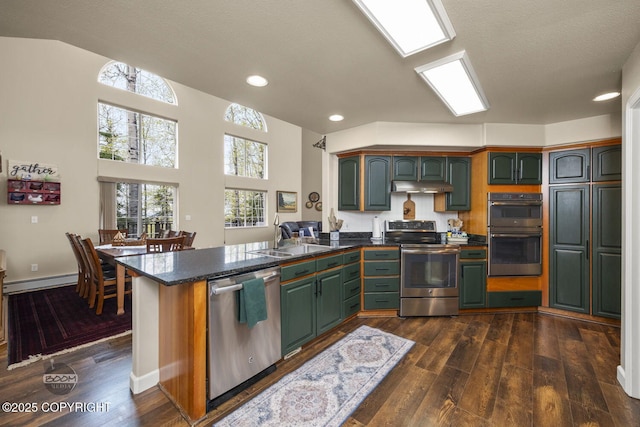kitchen with stainless steel appliances, a sink, a peninsula, dark countertops, and dark wood finished floors