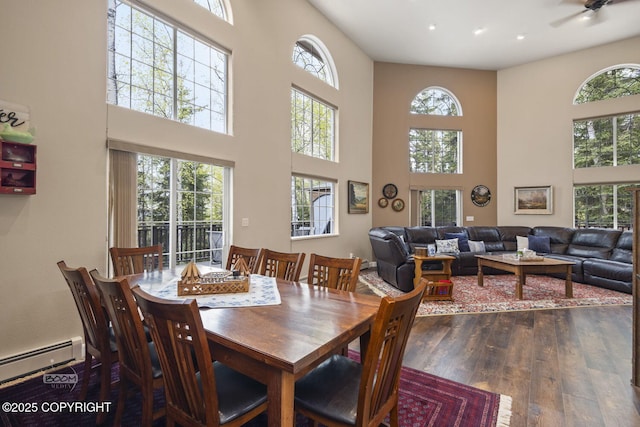 dining area with a baseboard heating unit, a high ceiling, wood-type flooring, recessed lighting, and a ceiling fan