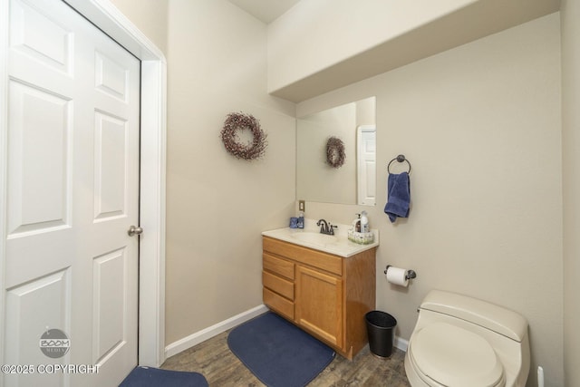 bathroom with baseboards, wood finished floors, vanity, and toilet