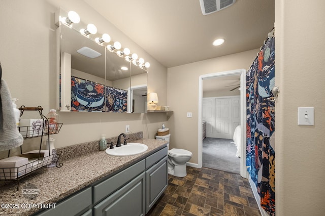 bathroom featuring stone finish flooring, vanity, toilet, a ceiling fan, and baseboards