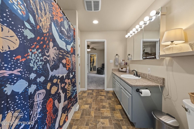 full bath featuring vanity, stone finish floors, baseboards, ceiling fan, and toilet