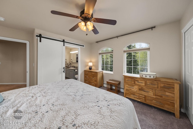 bedroom with a barn door, a sink, dark carpet, ceiling fan, and ensuite bath