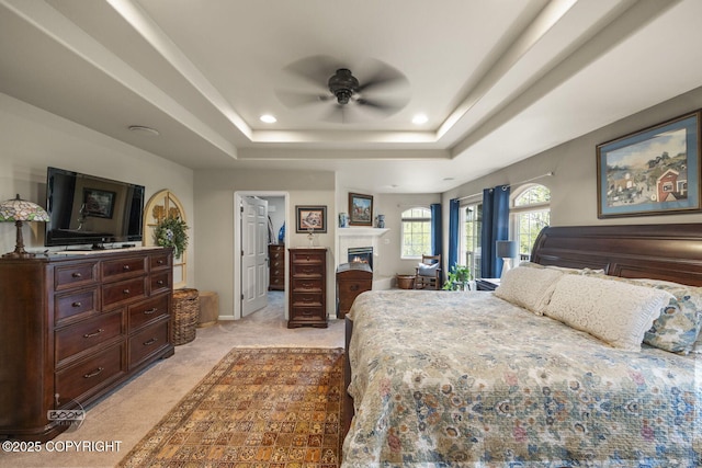 bedroom featuring light colored carpet, a tray ceiling, a lit fireplace, recessed lighting, and baseboards