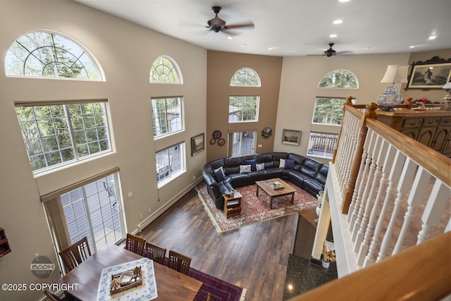 living area with a ceiling fan, recessed lighting, wood finished floors, a towering ceiling, and baseboards