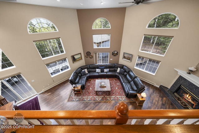 living room featuring wood finished floors, a high ceiling, a tile fireplace, ceiling fan, and baseboards