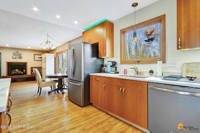 kitchen featuring appliances with stainless steel finishes, a sink, light countertops, light wood-style flooring, and open floor plan