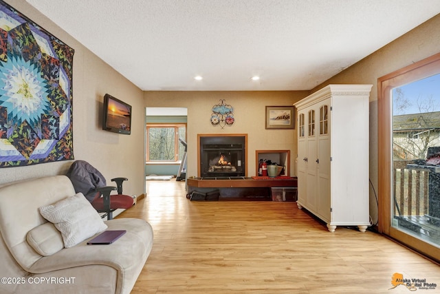 living room featuring recessed lighting, baseboards, a lit fireplace, and light wood-type flooring