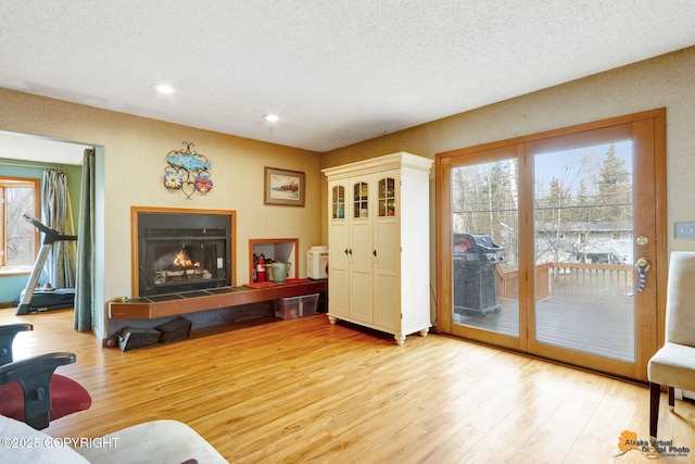living room featuring a warm lit fireplace, light wood-style flooring, a textured ceiling, and a wealth of natural light