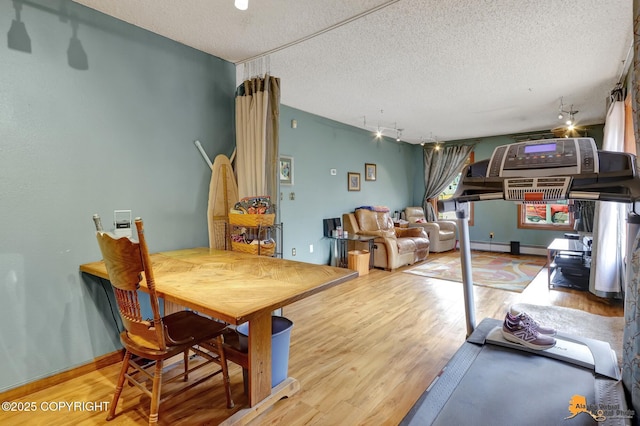 dining area with track lighting, a textured ceiling, a baseboard radiator, and wood finished floors
