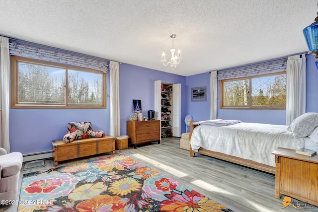 bedroom with a notable chandelier, a textured ceiling, wood finished floors, a spacious closet, and a baseboard heating unit