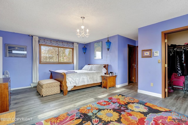 bedroom with a textured ceiling, a chandelier, wood finished floors, baseboards, and a spacious closet