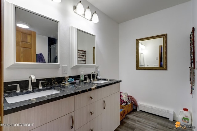 full bath with double vanity, a baseboard heating unit, a sink, and wood finished floors
