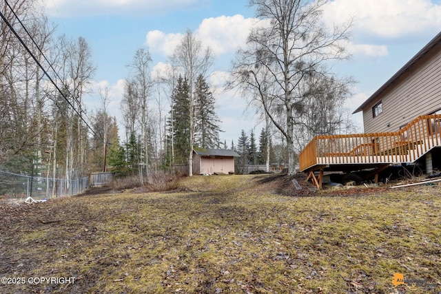 view of yard featuring a deck, fence, an outbuilding, and a shed