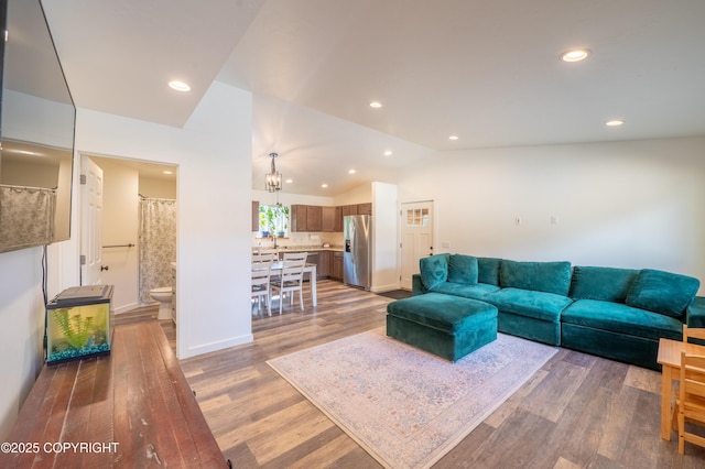 living area with vaulted ceiling, wood finished floors, recessed lighting, baseboards, and a chandelier