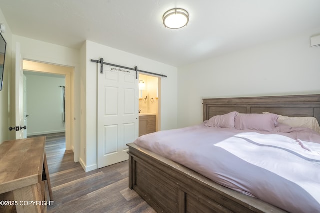 bedroom with dark wood-style floors, a barn door, baseboards, and connected bathroom