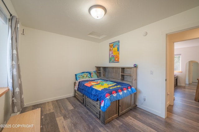 bedroom with wood finished floors, arched walkways, and baseboards