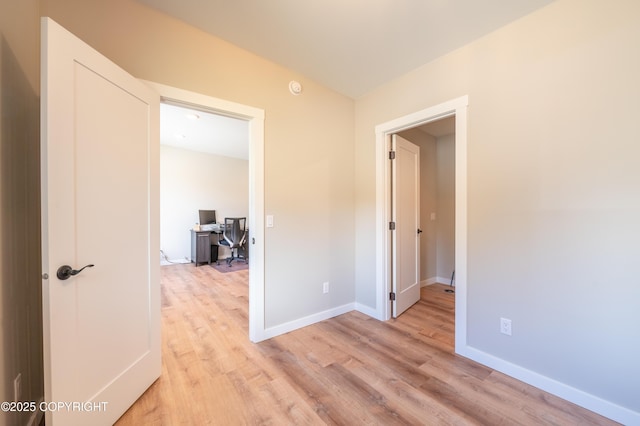 empty room featuring light wood-style floors, an office area, and baseboards