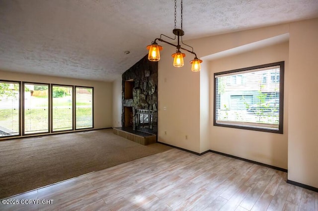 19532 Ostovia Cir, Eagle River, AK 99577 - unfurnished living room featuring baseboards, vaulted ceiling, a fireplace, a textured ceiling, and light wood finished floors