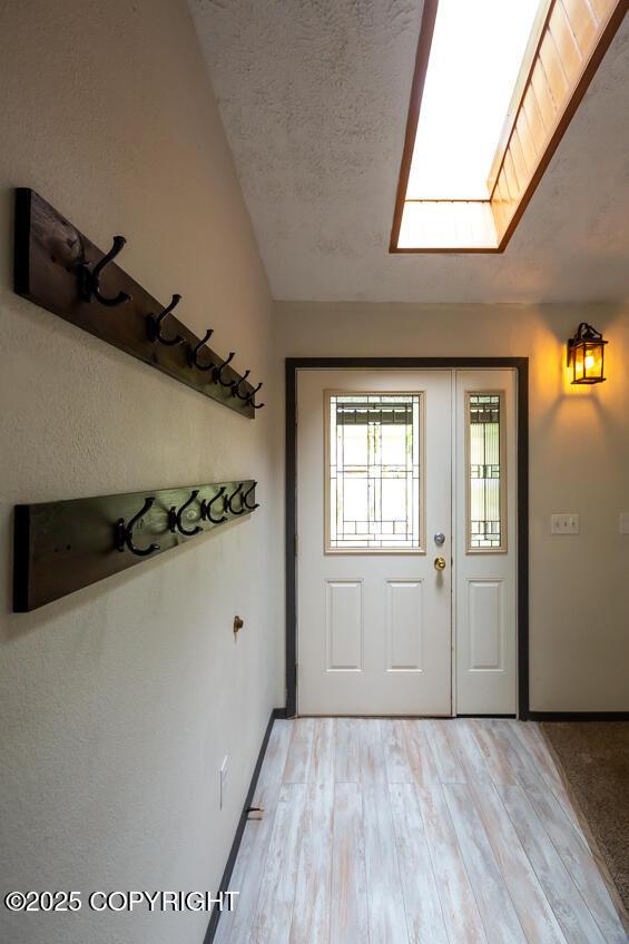 19532 Ostovia Cir, Eagle River, AK 99577 - doorway with vaulted ceiling with skylight, light wood-style flooring, baseboards, and a textured ceiling