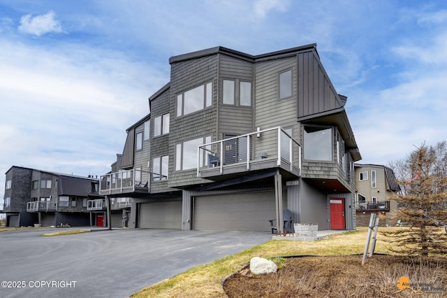 view of front of property featuring a garage, board and batten siding, a balcony, and aphalt driveway