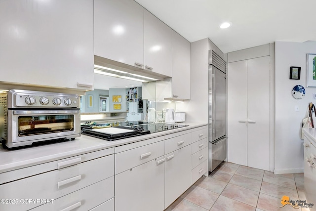 kitchen with light countertops, light tile patterned floors, stainless steel built in fridge, and black electric stovetop