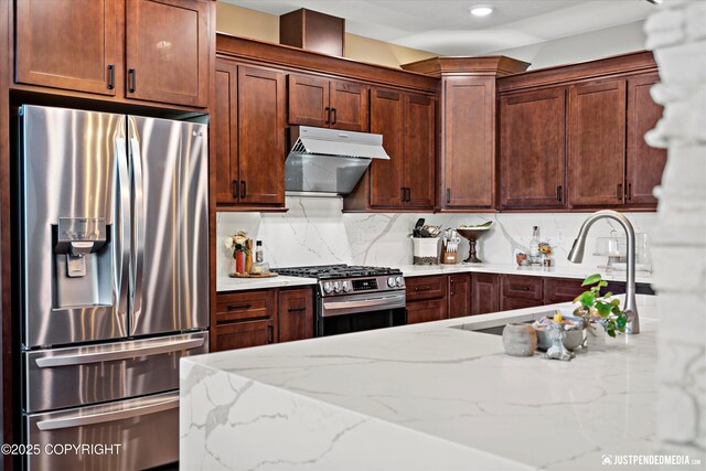 14009 W Big Lake Rd, Big Lake, AK 99652 - kitchen featuring appliances with stainless steel finishes, under cabinet range hood, light stone countertops, decorative backsplash, and a sink
