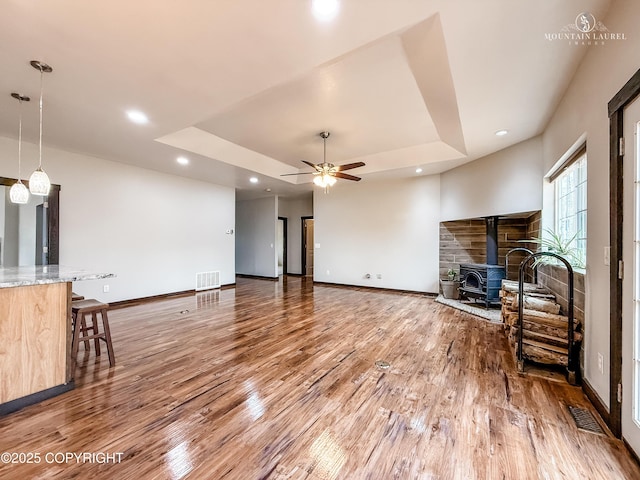 1340 N Rainbow Park Dr, Wasilla, AK 99623 - unfurnished living room with light wood-type flooring, a wood stove, a raised ceiling, baseboards, and visible vents