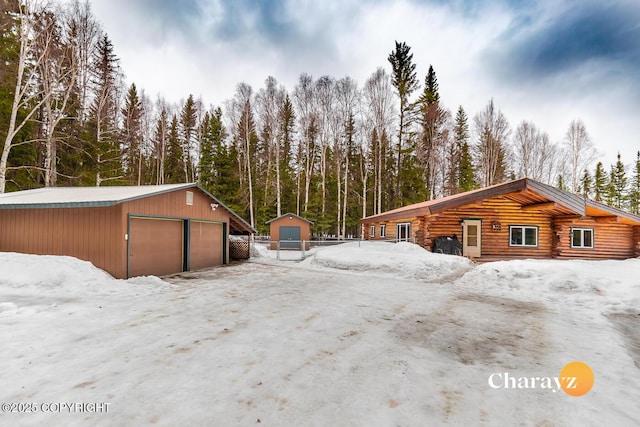 view of snow covered exterior featuring an outbuilding, a detached garage, and log exterior