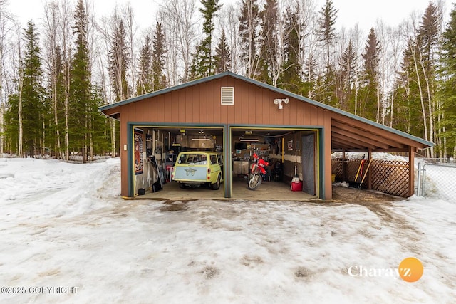 snow covered garage featuring a garage, a view of trees, and fence