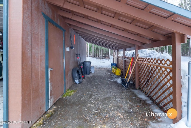 snow covered parking area featuring an attached carport and fence