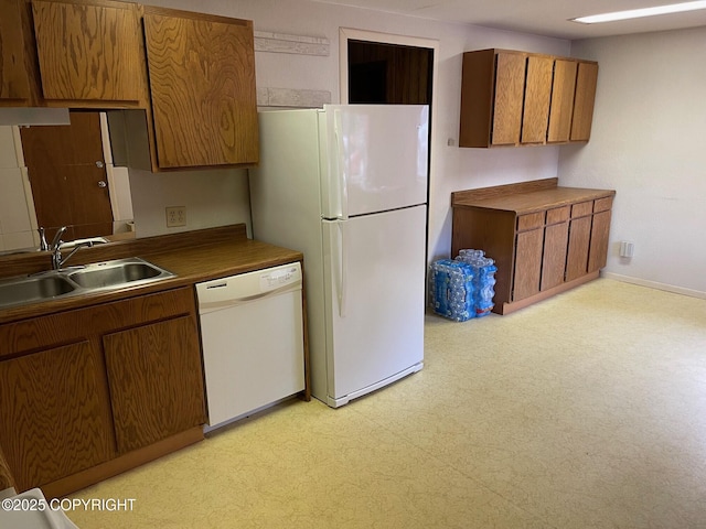 kitchen with brown cabinets, light floors, a sink, white appliances, and baseboards