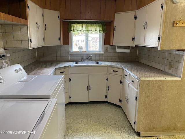 kitchen featuring white cabinets, light countertops, backsplash, a sink, and washing machine and clothes dryer