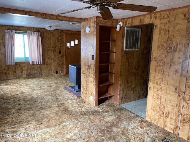 spare room featuring a wood stove, visible vents, wood walls, and ceiling fan