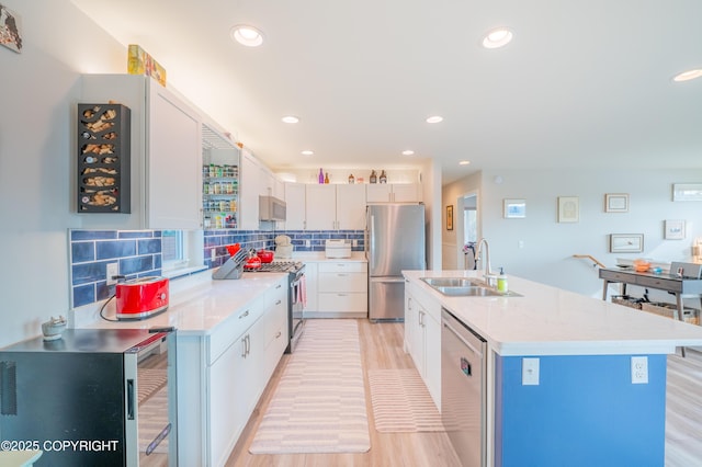 437 W Fairview Ave, Homer, AK 99603 - kitchen featuring appliances with stainless steel finishes, a sink, light wood-style flooring, decorative backsplash, and a center island with sink