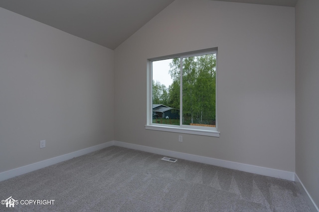 carpeted empty room featuring baseboards and vaulted ceiling
