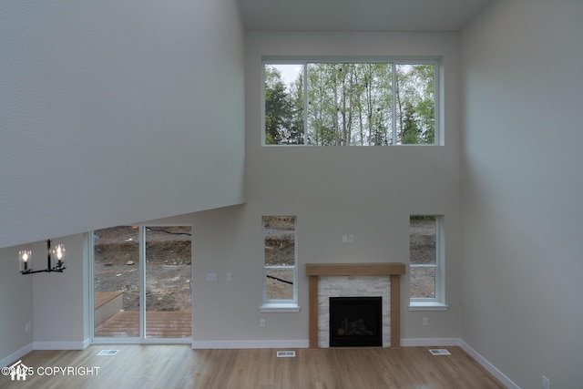 unfurnished living room with wood finished floors, a chandelier, a high ceiling, baseboards, and a fireplace