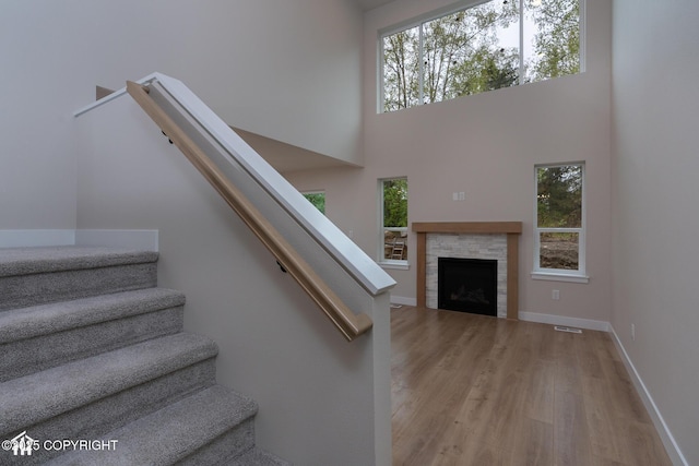 stairs with wood finished floors, healthy amount of natural light, baseboards, a towering ceiling, and a fireplace