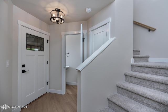 foyer entrance with stairs, wood finished floors, baseboards, and a chandelier