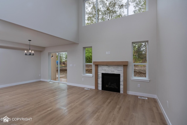 unfurnished living room with a chandelier, light wood-style floors, a fireplace, baseboards, and a high ceiling