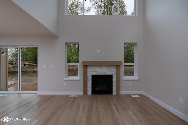unfurnished living room featuring a high ceiling, wood finished floors, baseboards, and a fireplace