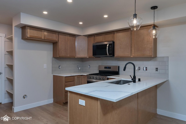 kitchen featuring stainless steel appliances, a sink, a peninsula, brown cabinets, and recessed lighting