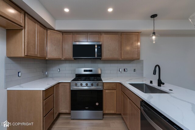kitchen featuring stainless steel appliances, a sink, light wood-style flooring, light stone counters, and decorative backsplash