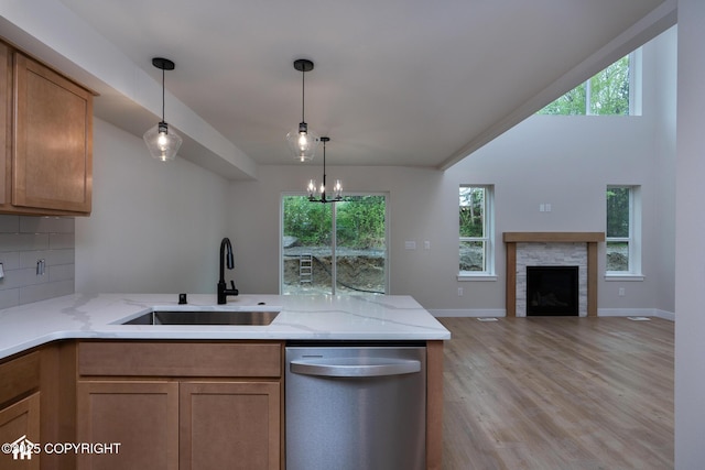 kitchen featuring stainless steel dishwasher, a sink, a peninsula, light wood finished floors, and light stone countertops