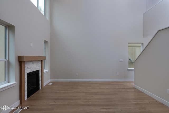 unfurnished living room with wood finished floors, a fireplace, baseboards, and a towering ceiling