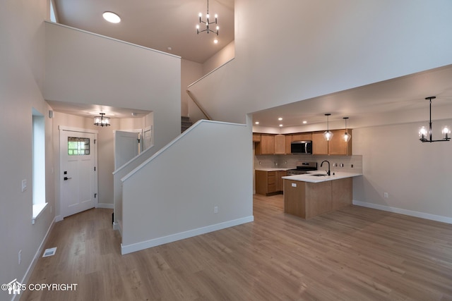 kitchen with a chandelier, appliances with stainless steel finishes, brown cabinets, light countertops, and light wood finished floors