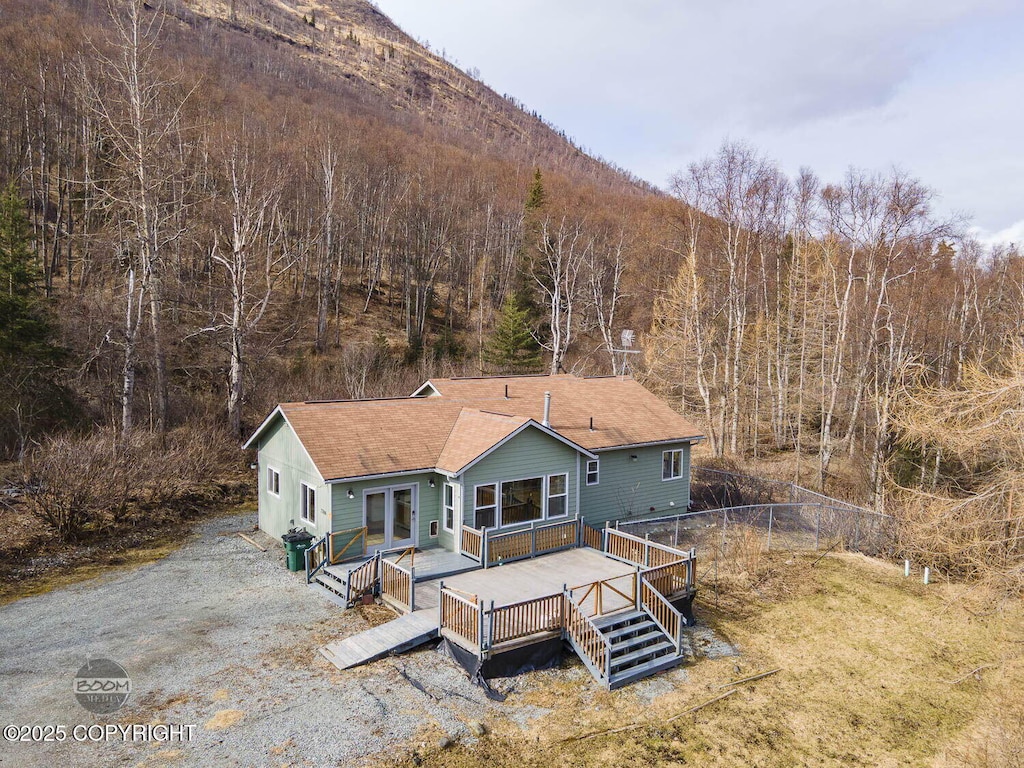 back of house featuring fence, a wooden deck, a forest view, and roof with shingles