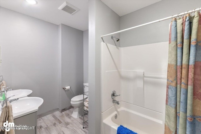 bathroom featuring double vanity, toilet, wood finished floors,  shower combination, and visible vents