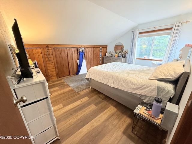bedroom featuring lofted ceiling, wooden walls, and wood finished floors