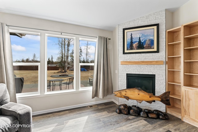 interior space featuring a fireplace, visible vents, vaulted ceiling, baseboards, and wood finished floors